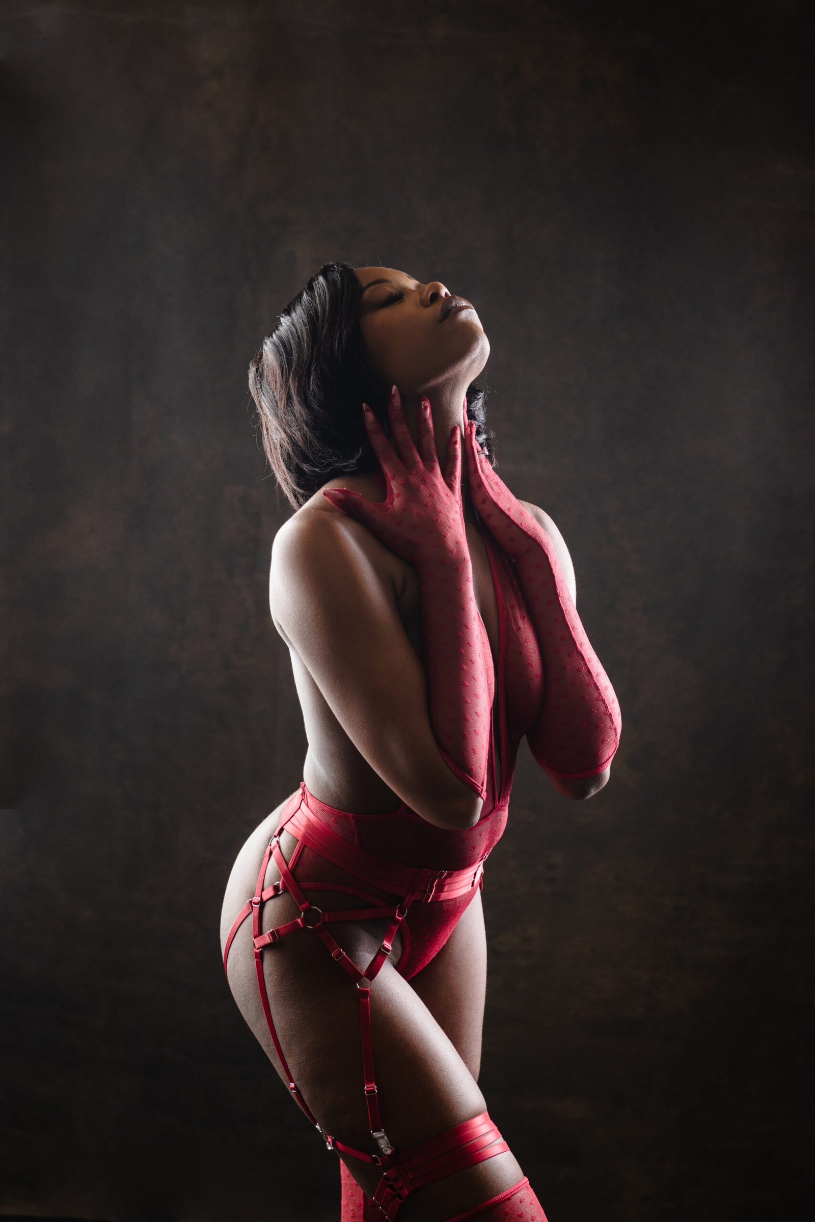 Woman in red bodysuit, artistic boudoir photo against dark background, Bare By M